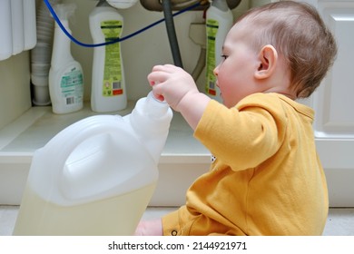 Toddler Baby Boy Is Playing With Detergents And Cleaning Products In An Open Kitchen Cabinet. Child Safety Issues In The Home Room, Little Kid