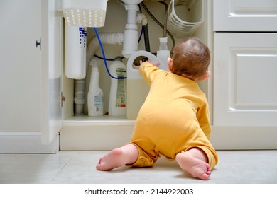 Toddler Baby Boy Is Playing With Detergents And Cleaning Products In An Open Kitchen Cabinet. Child Safety Issues In The Home Room, Little Kid