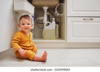 Toddler Baby Boy Is Playing With Detergents And Cleaning Products In An Open Kitchen Cabinet. Child Safety Issues In The Home Room, Little Kid