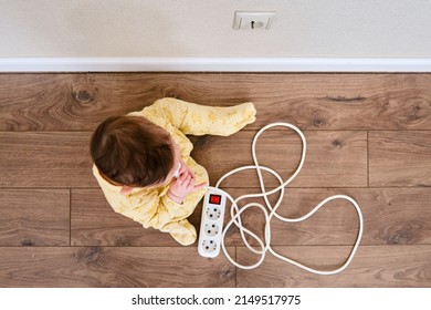 Toddler baby boy plays with electric wires while sitting on the floor. Child holding an extension cord with electrical sockets