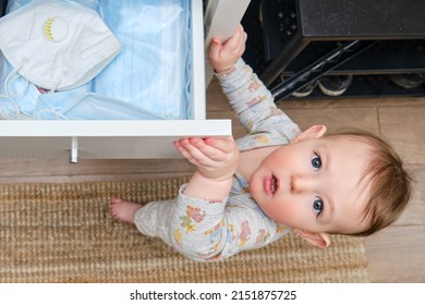 Toddler Baby Boy Rips Open A Drawer Of A Closet Full Of Medical Face Masks During The Coronavirus Pandemic. The Child Holds The Cabinet Door Handle, A Small Kid