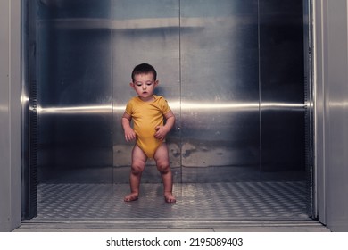 Toddler Baby Boy Stands Alone In The Elevator Of A Residential Building. A Child In An Elevator With The Doors Open. Kid Age One Year