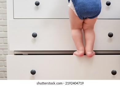 Toddler Baby Climbed Up On The Open Chest Of Drawers. Child Boy Stood On A Tall Drawer Of A White Cabinet. Kid Age One Year