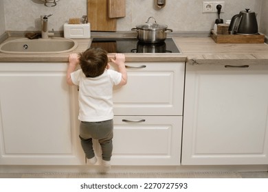 Toddler baby climbs on a hot electric stove in the home kitchen. A small child touches the surface of the stove with his hand at the risk of getting burned. Kid aged one year eight months - Powered by Shutterstock