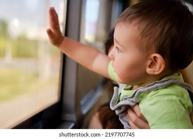Toddler Baby Looks Out The Bus Window While Sitting In The Arms Of His Mother. Child In Transport With A Parent, Close-up