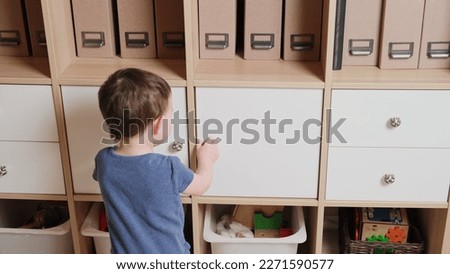 Toddler baby opens the closet door in the home living room. A small child opens a shelf drawer. Kid aged one year eight months