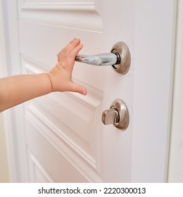 Toddler baby opens the door holding the door handle, child hand close-up. White wooden door, metal door handle and baby hand - Powered by Shutterstock