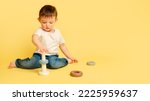 Toddler baby is playing logic educational games with a pyramid on a studio yellow background. Happy child playing with a pyramid toy, learning logic, copy space. Kid aged one year and four months