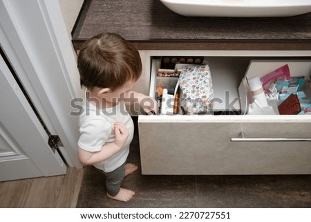 Toddler baby pulls out an item drawer in a home bathroom. A small child explores the closet in the bathroom. Kid aged one year eight months
