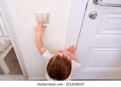 Toddler Baby Reaches For The Light Switch, Child Hand Turns On The Lamp Close-up. White Light Switch In Home Room And Baby Hand