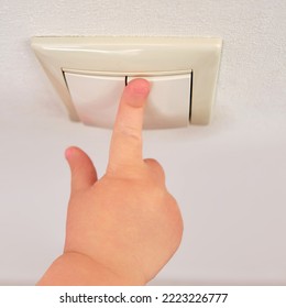 Toddler Baby Reaches For The Light Switch, Child Hand Turns On The Lamp Close-up. White Light Switch In Home Room And Baby Hand