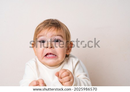 Toddler baby sitting on the high chair and doing funny grimace. Teeth of the baby. Face expression