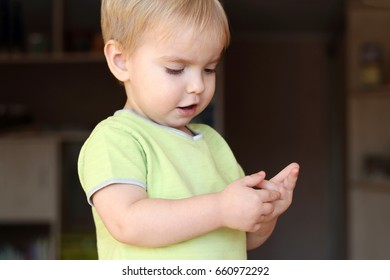 A Toddler Blond Boy Looking Musingly And Thoughtfully And Counting His Fingers, Close-up Emotional Portrait, Sign And Gesture Concept