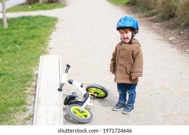 Toddler Boy Crying Because He Fell Off The Bike While Riding At Pump Track. Little Baby About 2 Years Old Learning And Beginner Racing Bicycle. Child With Safety Helmet Playing With Balance Bike.