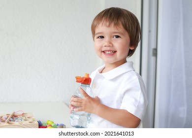 Toddler boy drinking water on white background. Baby holding soft drink plastic bottle. Mixed race Asian-German child about 2 years old.