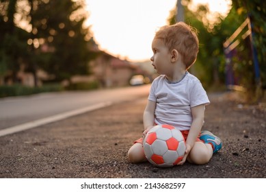 A Toddler Boy With A Football Ball On The Street.	