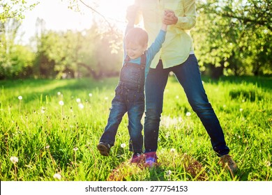 Toddler boy and his mom having fun in summer park, Image with backlight, some stay light in foreground