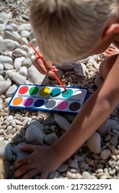 Toddler Boy Painting Rocks With Water Colors On The Pebble Beach On A Summer Day.