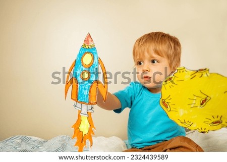 Toddler boy play astronaut holding paper rockets and planets at home with expression making sound of liftoff