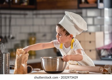 Niño pequeño jugando con la masa en la cocina vestido de chef. Preparando un pastel para niños
