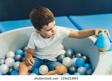 Toddler Boy Playing With A Toy While Sitting In A Ball Pit Full Of Colorful Balls. A Ball Pit - A Great Place For Kids To Jump, Crash, And Wiggle. Sensory Play At The Nursery School. High Quality