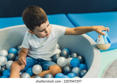 Toddler Boy Playing With A Toy While Sitting In A Ball Pit Full Of Colorful Balls. A Ball Pit - A Great Place For Kids To Jump, Crash, And Wiggle. Sensory Play At The Nursery School. . High Quality