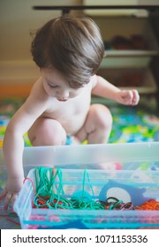 Toddler Boy Plays In Sensory Bin Of Colored Spaghetti