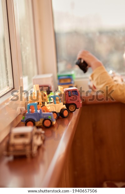 Toddler boy\
plays with toy cars near the window. Models of multi-colored cars\
in a row. Children\'s pastime\
concept