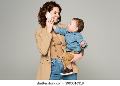 toddler boy reaching smartphone while happy mother in blazer talking isolated on grey - Powered by Shutterstock