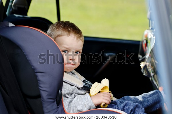 \
toddler boy sitting in the car seat and eating a\
banana
