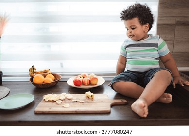 Toddler boy sitting on a kitchen counter preparing a healthy fruit snack