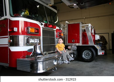 Toddler Boy Sitting On And Looking At A Firetruck..