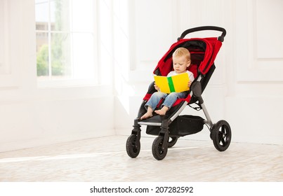 Toddler boy sitting in stroller at home and looking at open book