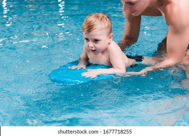 Toddler Boy Swimming With Flutter Board Near Swim Coach