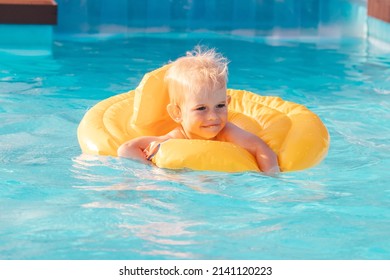 Toddler Boy Swimming With Inflatable Floatie In Swimming Pool On A Sunny Day.