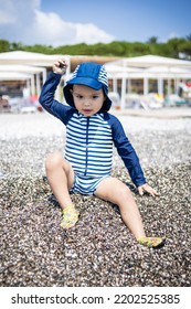 Toddler Boy In A Swimming Suit Plays With Pebbles On The Seashore In Hotel