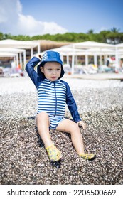 Toddler Boy In A Swimming Suit Plays With Pebbles On The Seashore In Hotel