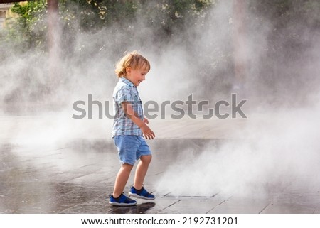 Toddler boy under spray jets of extensive water mirror fountain in Nice, France. Pleasant refreshment , stay coll in summer heat.