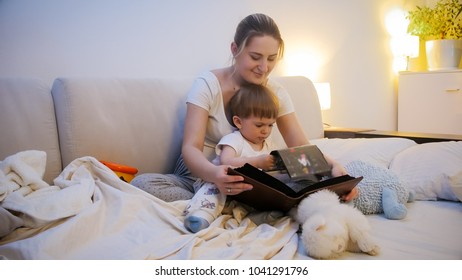 Toddler Boy Watching Family Photo Album With His Mother In Bed At Night