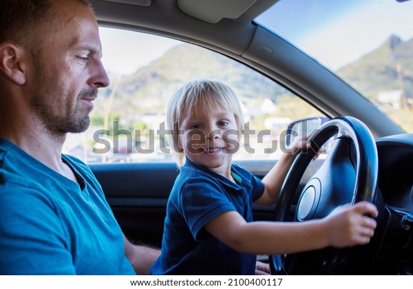 Toddler child, boz, sitting in fathers lap and\
pretending to drive a\
car