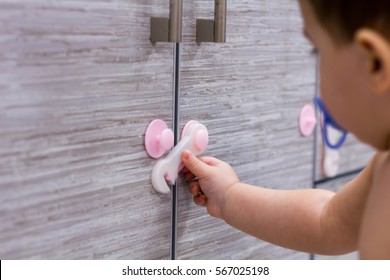 Toddler Child In Kitchen, Children Safety At Home Concept. Flexible Latch On The Cabinet. Little Baby Playing With Drawer Unrecognizable