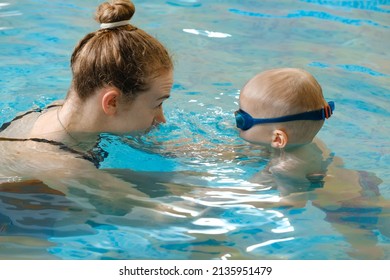 Toddler Child Learning To Swim In Indoor Swimming Pool With Teacher. Floating In The Water, Balancing And General Physical Activity For Kids, Early Development. Boy Kid Trained To Kick Legs And Float