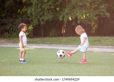 Toddler Children, Boy And Girl, Playing Soccer Together At Football Field. Little Friends Kicking Ball In Summer Day Standing At Stadium In Sun Light. Friendship And Sports For Kids Concept