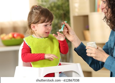 Toddler crying at lunch time sitting in a highchair in the living room at home with a homey background