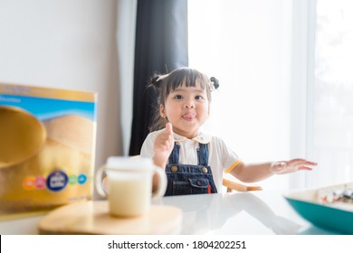 Toddler Cute Little Asian Girl Drinking Milk At Table In Kitchen.Thumb Up For Good Milk.Cute Baby Girl Drinking Milk With Milk Mustache At Home.Concept For Food, Growth In Kid, Child Development.