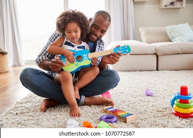 Toddler daughter sits on dads knee playing ukulele at home - Powered by Shutterstock