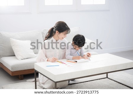 A toddler enjoys learning while opening a notebook under Mom's watchful eye Enjoying activities like drawing and coloring together,wide angle