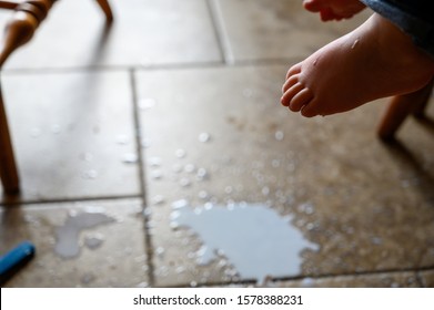 Toddler Foot Suspended Above Spilled Milk, Crumbs, And A Plastic Fork On A Brown Tile Floor 