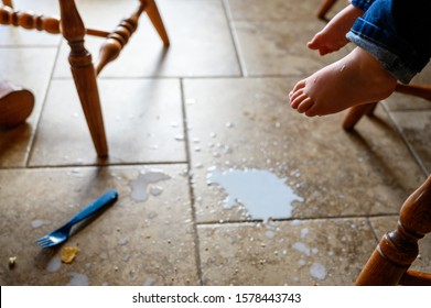 Toddler Foot Suspended Above Spilled Milk, Crumbs, And A Plastic Fork On A Brown Tile Floor 