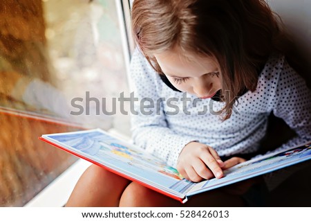 toddler girl with book near the window
